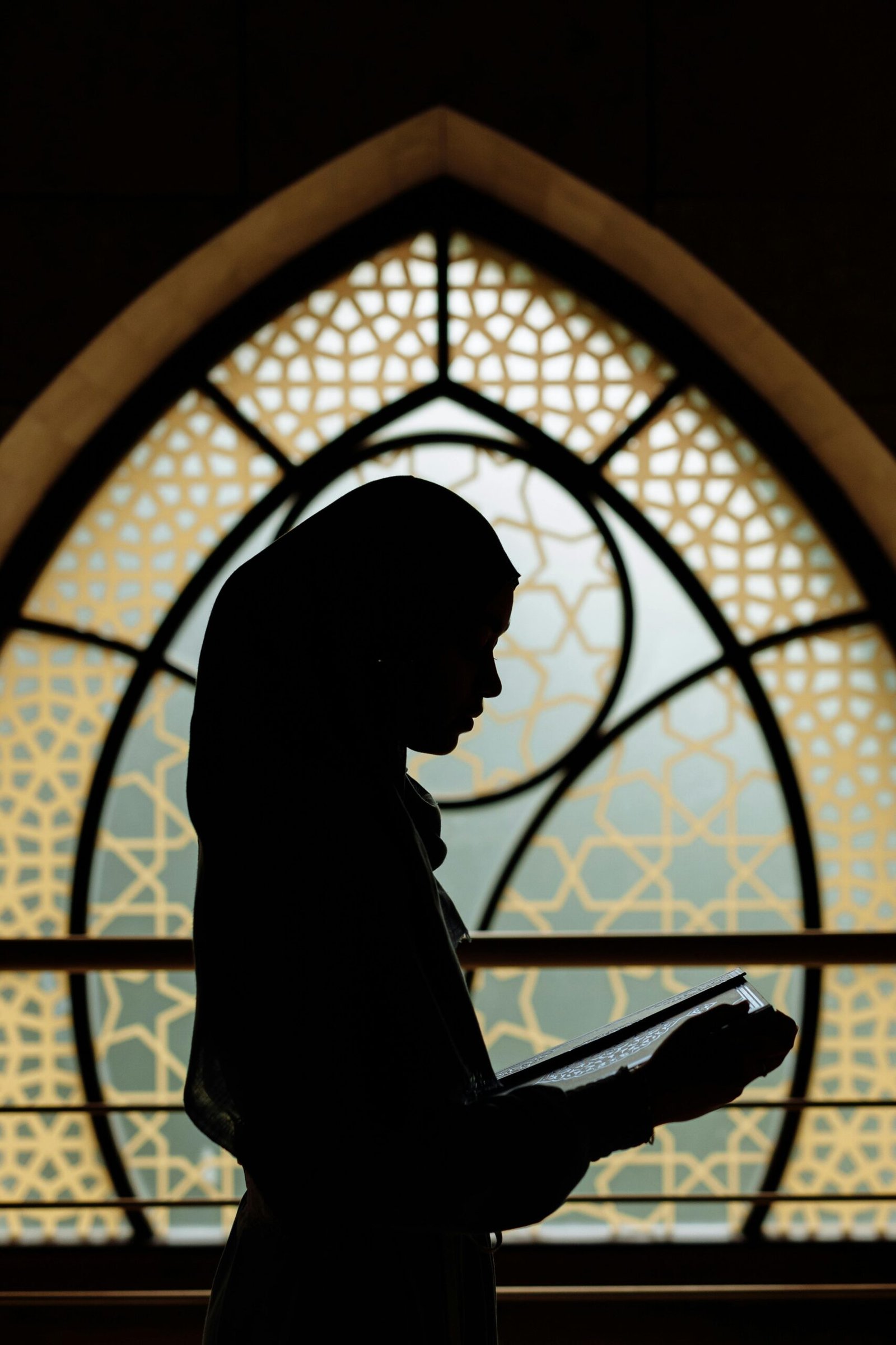 Silhouette of a woman reading in front of Islamic-patterned window. Peaceful and cultural ambiance.