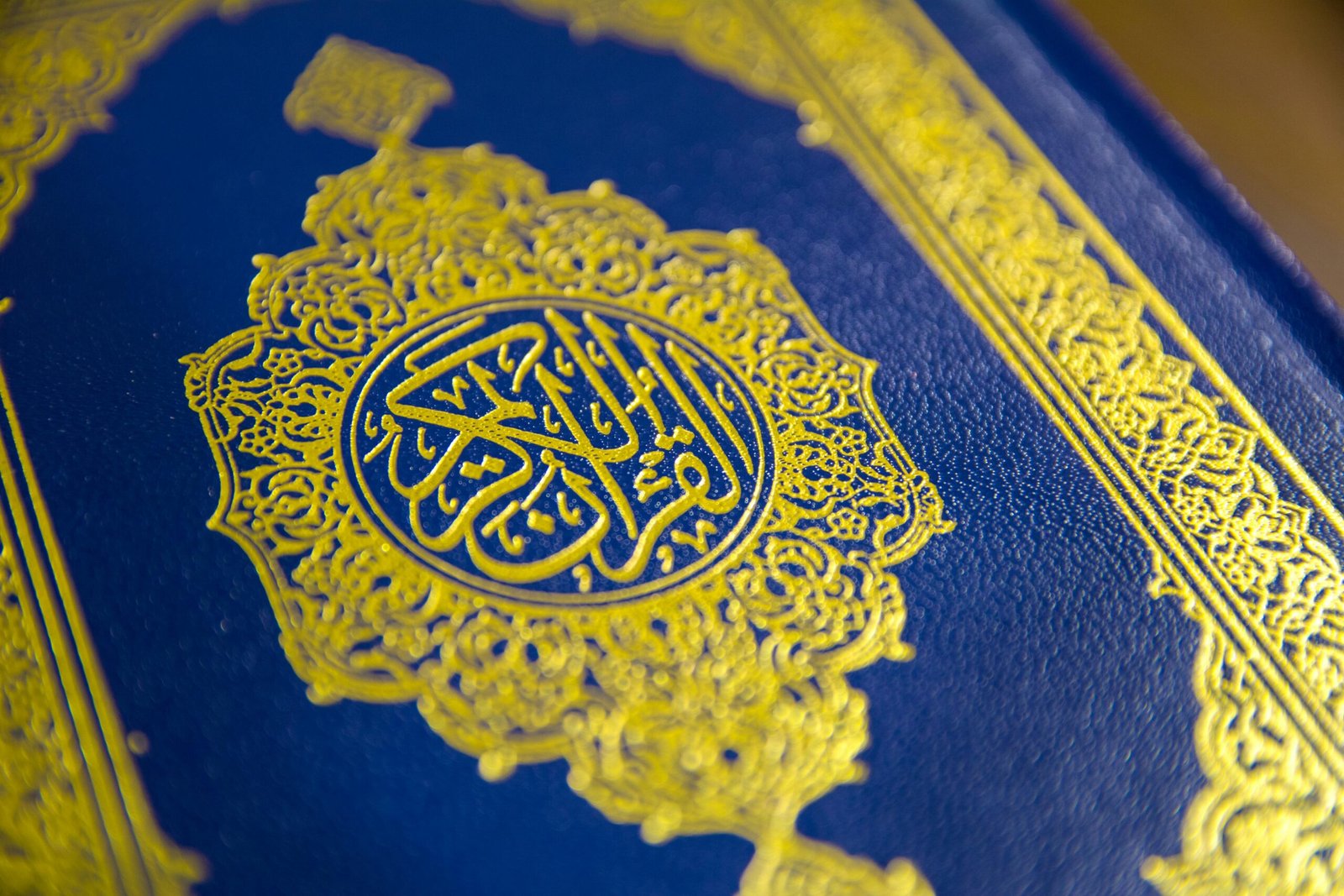 Close-up of intricate gold Quranic calligraphy on a blue cover, showcasing elegant Islamic design.